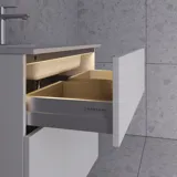 Stijlvolle badkamer inspiratie met beige wastafelmeubel met binnenlade, bovenkast, open plank, ovale spiegel met verlichting, bijpassende hanglampen, plank onder de spiegel en wandgemonteerd toilet. Wanden met lichte, langwerpige tegels