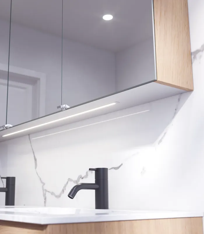 Badkamerinspiratie met wastafelkasten en bovenkasten in licht eikenhout met groeven, elegante dubbele wastafel, mooie spiegelkast met verlichting, visgraatvloer in licht hout en witte marmeren muur geven een klassieke, lichte en strakke uitstraling.