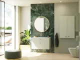 Stijlvolle en luxueuze badkamer met zachte groene tinten, een grote elegante ronde spiegel en een modern, verfijnd groen toilet