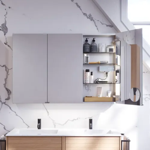 Badkamerinspiratie met wastafelkasten en bovenkasten in licht eikenhout met groeven, elegante dubbele wastafel, mooie spiegelkast met verlichting, visgraatvloer in licht hout en witte marmeren muur geven een klassieke, lichte en strakke uitstraling.