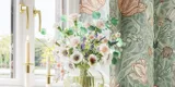 Badkamerinspiratie met groene meubels in speciale kleur met zijden van natuurlijk eikenhout, elegante groeven, werkblad met ovale opzetwastafel, ovale spiegel en bloemenbehang geeft een sierlijke, retro uitstraling.