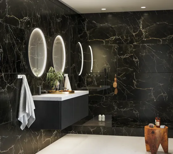 Elegante en moderne badkamer inspiratie met donkere marmeren muren, ronde verlichte spiegels met zwarte rand, wandgemonteerde wastafelkast met dubbele wastafel en een ruime douchehoek