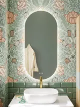Badkamerinspiratie met groene meubels in speciale kleur met zijden van natuurlijk eikenhout, elegante groeven, werkblad met ovale opzetwastafel, ovale spiegel en bloemenbehang geeft een sierlijke, retro uitstraling.