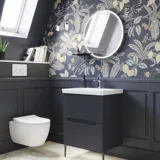 Badkamerinspiratie met donkerblauwe wandpanelen, romantisch bloemenbehang, donkerblauw wastafelmeubel met zachte vormen en een prachtige ronde spiegel met licht dat een vintage uitstraling creëert