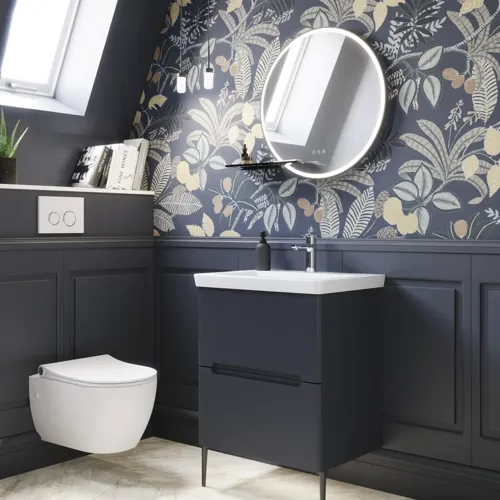 Badkamerinspiratie met donkerblauwe wandpanelen, romantisch bloemenbehang, donkerblauw wastafelmeubel met zachte vormen en een prachtige ronde spiegel met licht dat een vintage uitstraling creëert