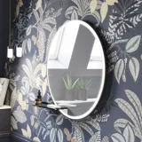 Badkamerinspiratie met donkerblauwe wandpanelen, romantisch bloemenbehang, donkerblauw wastafelmeubel met zachte vormen en een prachtige ronde spiegel met licht dat een vintage uitstraling creëert