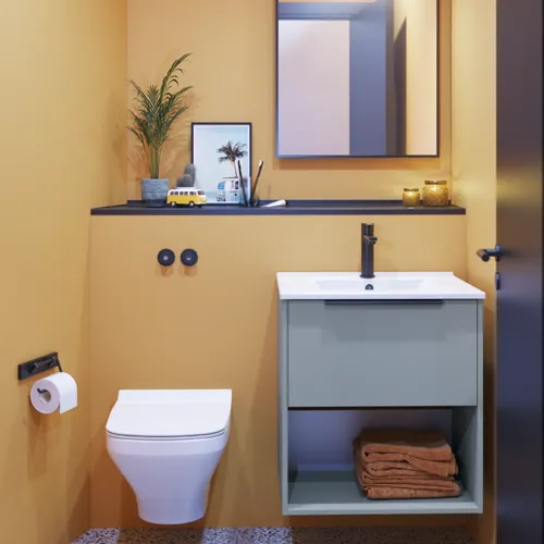 Kleine badkamerinspiratie met schuine en warme gele muren, elegant lichtblauw wastafelmeubel, dunne en strakke wastafel en een minimalistische vierkante spiegel met zwarte rand en praktische lamp.