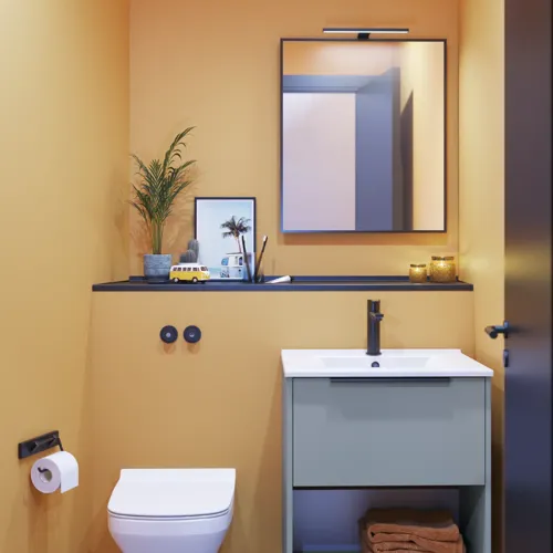 Kleine badkamerinspiratie met schuine en warme gele muren, elegant lichtblauw wastafelmeubel, dunne en strakke wastafel en een minimalistische vierkante spiegel met zwarte rand en praktische lamp.