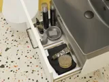 Kleine badkamerinspiratie met een wit wastafelkastje met zwarte greep en zwarte elegante wastafel, mooie ronde spiegel met zwarte rand, verschoven wandkasten en een terrazzo wand en vloer en gele muren geven een gedurfde en moderne uitstraling.