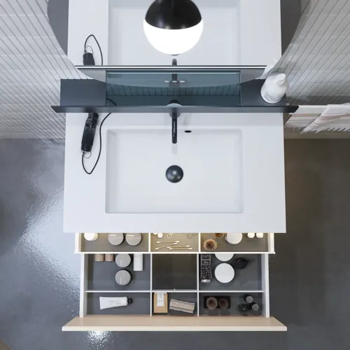 Stijlvolle badkamer inspiratie met beige wastafelmeubel met binnenlade, bovenkast, open plank, ovale spiegel met verlichting, bijpassende hanglampen, plank onder de spiegel en wandgemonteerd toilet. Wanden met lichte, langwerpige tegels.