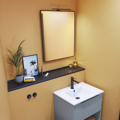 Kleine badkamerinspiratie met schuine en warme gele muren, elegant lichtblauw wastafelmeubel, dunne en strakke wastafel en een minimalistische vierkante spiegel met zwarte rand en praktische lamp.