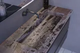 Grote badkamerinspiratie met grijs badmeubel met geïntegreerde handgreep, stijlvolle wastafel aan de zijkant, vierkante spiegel met afgeronde hoeken, betonlook muren en ruwe materialen voor een urban look