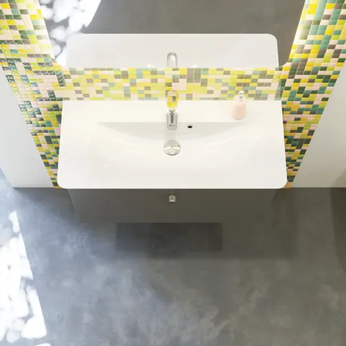 Badkamerinspiratie met badkamermeubels in mat grijs met elegante wastafel, mooie vierkante spiegel, grijze vloer en kleine tegels in verschillende tinten geel en groen, die met de gele muur een heldere en speelse uitdrukking geven