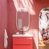 Badkamerinspiratie met rode muren, zacht gevormde rode wastafelmeubel en hoge kast, elegante witte wastafel en een prachtige ovale spiegel met licht die samen met de natuurlijke omgeving een vintage uitstraling creëren